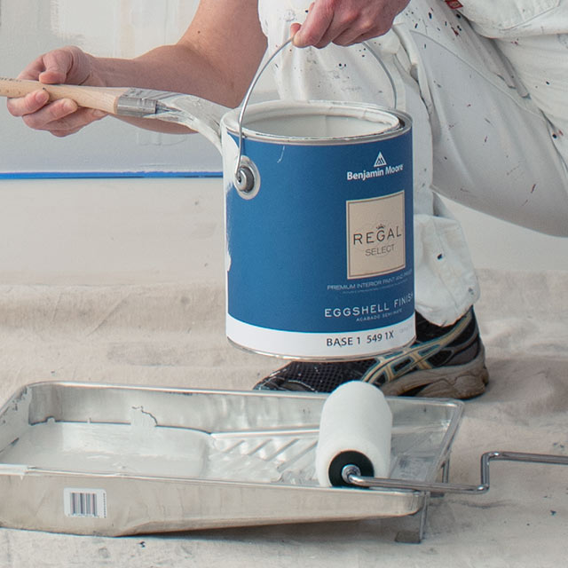 A contractor loads a roller tray with Benjamin Moore® paint