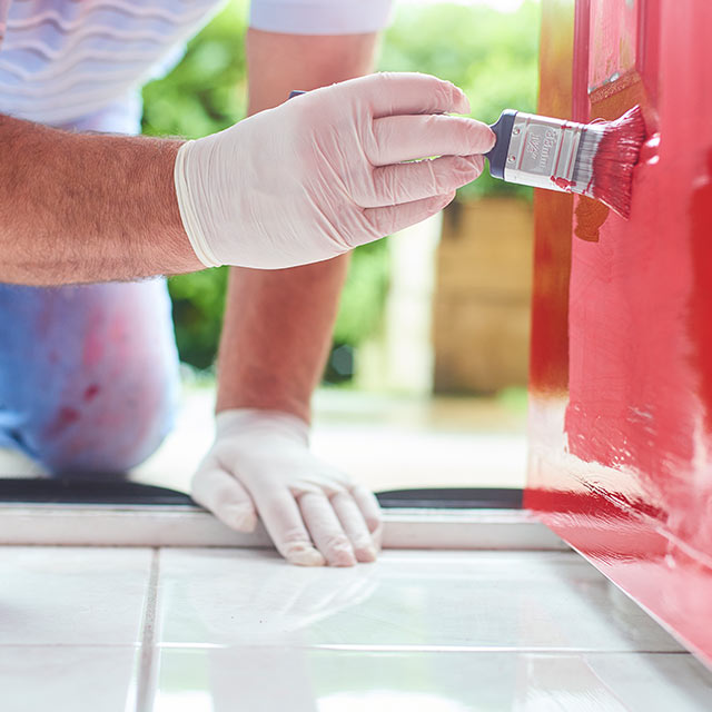 Un entrepreneur de Benjamin Moore peint une porte d’entrée en rouge.