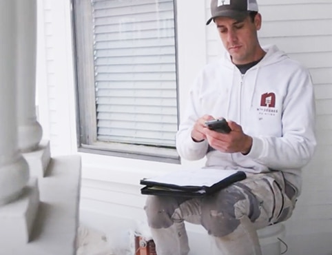 A painting contractor sitting in front of a white house using his cell phone to manage his business.