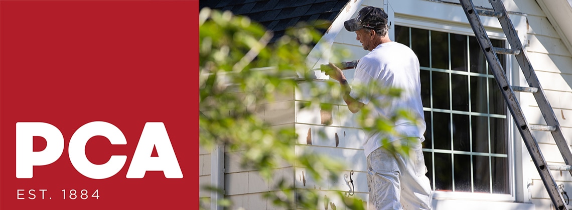 A painting contractor using a caulking gun on the exterior of a white painted house.