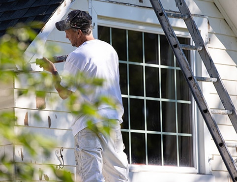 A painting contractor using a caulking gun on the exterior of a white painted house.