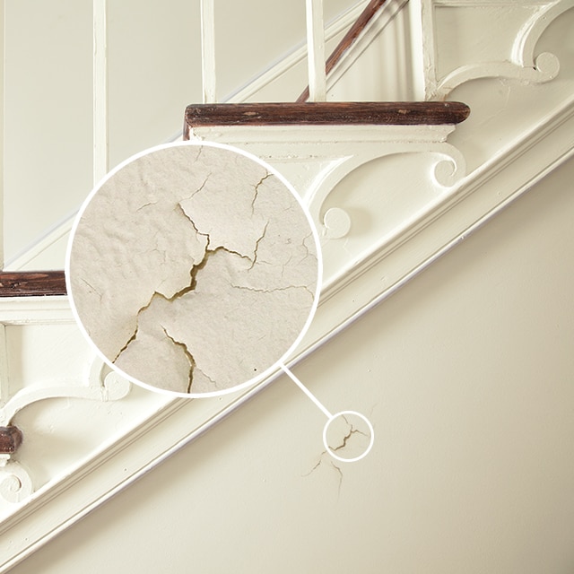 A close-up that shows paint cracking and flaking on a wall beneath a staircase.