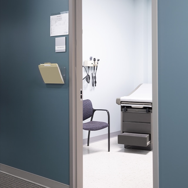 A blue painted-hallway with gray trim in a medical office, looking into a pristine exam room.