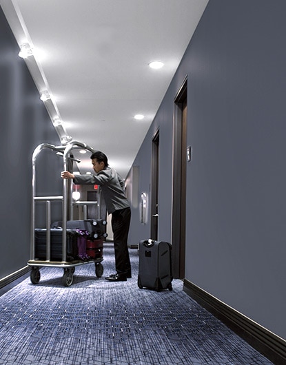 A bellhop unpacks bags from a luggage cart in a hotel hallway where scuffing can be an unsightly problem.