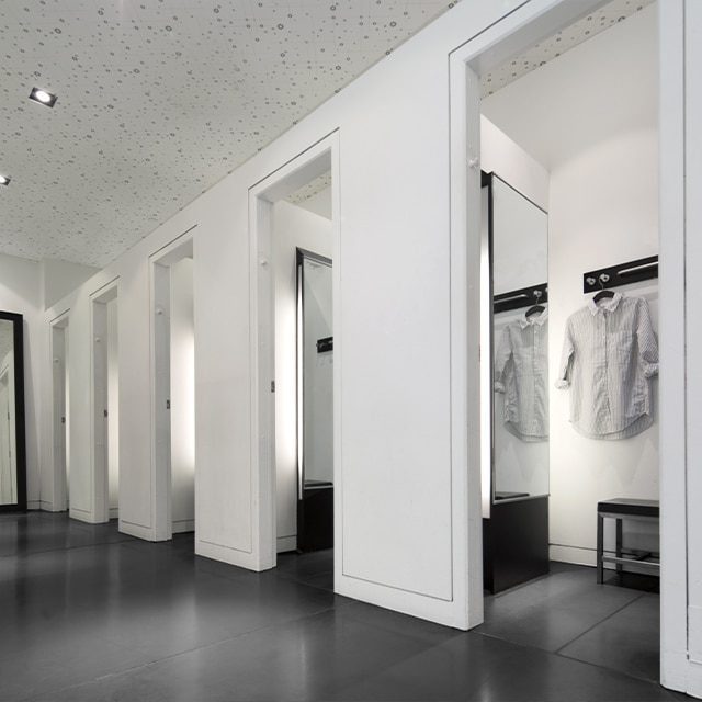 Une aire d’essayage peinte en blanc sans aucune marque de frottement avec des portes ouvertes, des miroirs et un plancher noir.