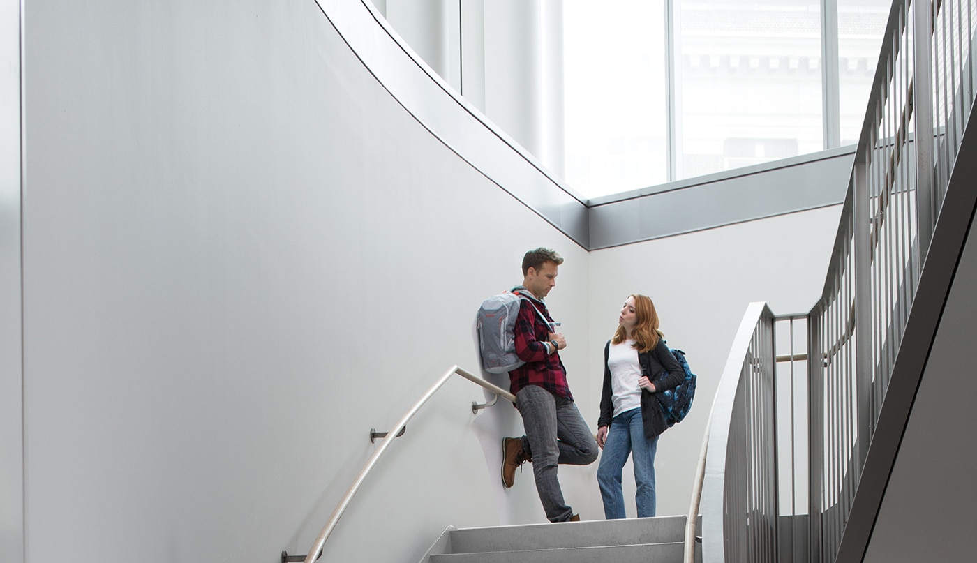 A multi-story staircase with gray-painted walls, large windows, and a man and woman standing on the landing.