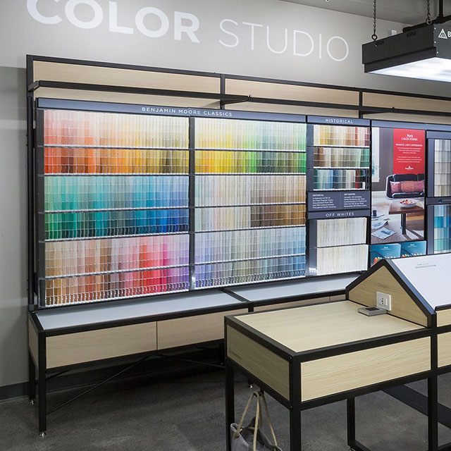 The interior of a Benjamin Moore store features a color display and a range of products on shelving.