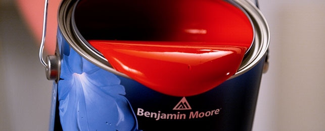 Benjamin Moore blue tin paint Can with opened lid and pouring out the red colored paint.