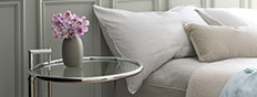 A gray bedroom wall with a glass bedside table