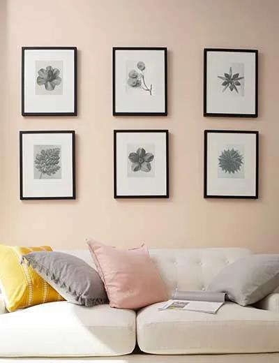Una pared rosa claro con cuadros y un sofá.