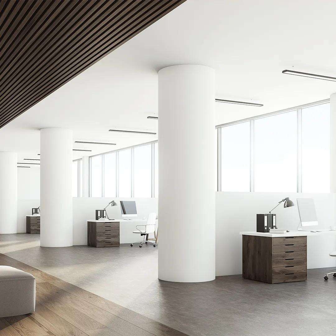 Un espacio de oficina con interiores pintados de blanco, grandes columnas, cubículos y ventanas.