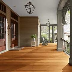 Miniatura de un espacioso porche delantero cubierto con revestimientos exteriores pintados de color Beige, columnas de color Verde apagado y techo Blanco, que cuenta con hermosas puertas principales y piso teñido con Woodluxe® Tinte para exteriores Traslúcido en Teca ES-30.