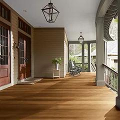 Miniatura de un espacioso porche delantero cubierto con revestimientos exteriores pintados de color Beige, columnas de color Verde apagado y techo Blanco, que cuenta con hermosas puertas principales y piso teñido con Woodluxe® Tinte para exteriores Traslúcido en Marrón Castaña ES-65.