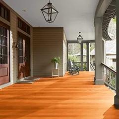 Miniatura de un espacioso porche delantero cubierto con revestimientos exteriores pintados de color beige, columnas de color verde apagado y techo blanco, que cuenta con hermosas puertas principales y piso teñido con Woodluxe® Tinte para exteriores Traslúcido en Redwood ES-20.