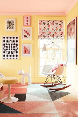 Un divertido dormitorio pintado en tonos vibrantes, que incluye un techo de color rosa suave y paredes de color amarillo claro, una silla mecedora, persianas con patrón de durazno y una variedad de almohadas y arte gráficamente audaces y coloridos.