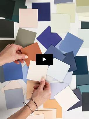 Las manos ordenan pequeños cuadrados de muestras de colores de pintura, la mayoría en tonos de azul y colores neutros.