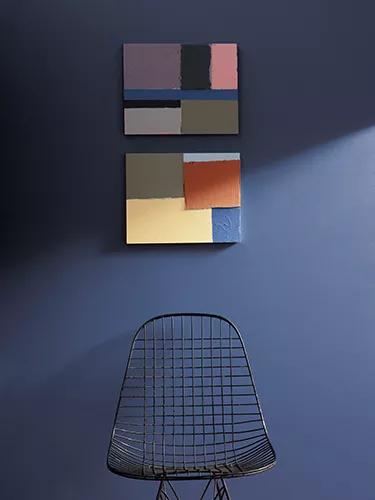 Una pared en azul profundo con arte que representa los ocho colores de la paleta del color del año de Benjamin Moore y una silla de metal negra en forma de cesta.