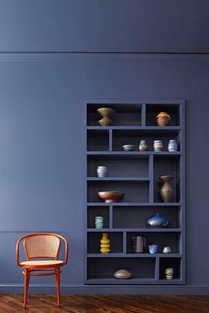 Un espacio sereno con estanterías empotradas y toda la pared pintada de azul profundo, con una pequeña silla de cuero estilo club.