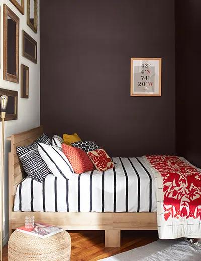 Un rincón de la habitación con paredes en matices chocolate intenso y una pared de galería blanca por encima de una cama.