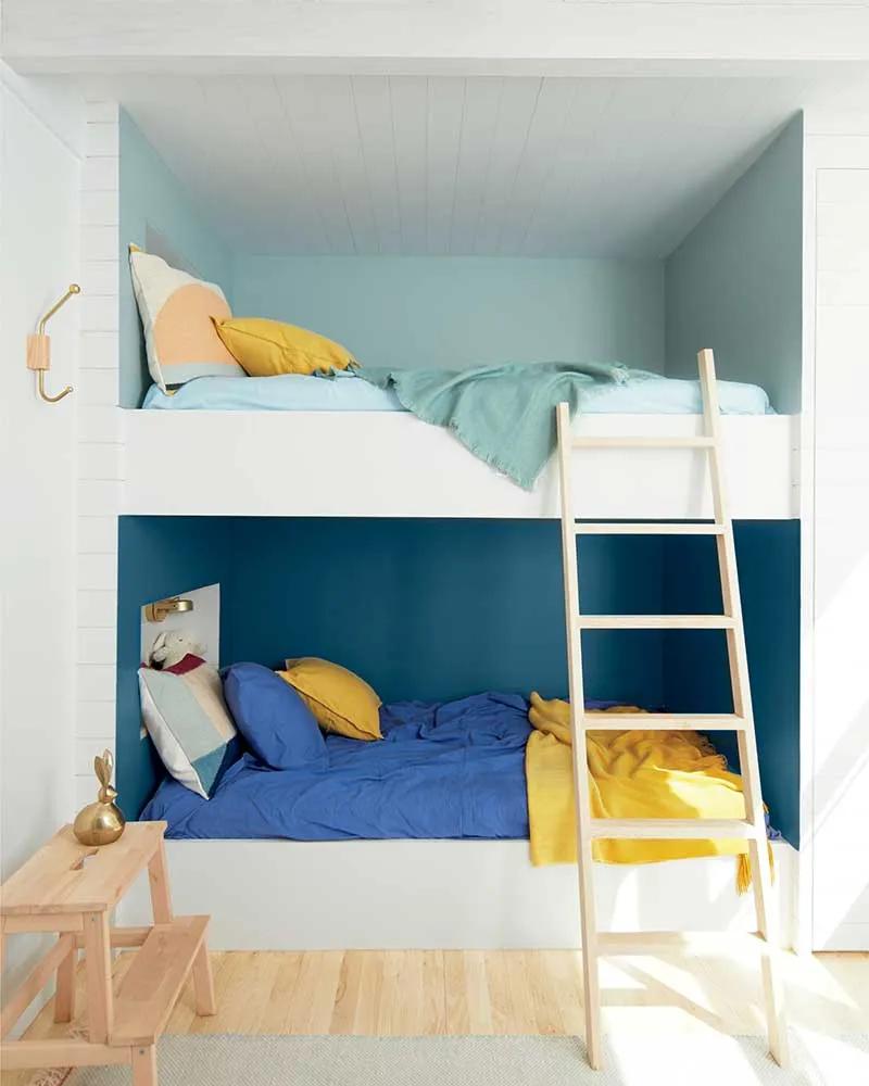 Una habitación blanca con paredes de litera pintadas en tonos azules y ropa de cama a juego.