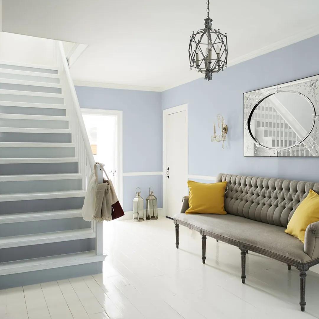 Un vestíbulo pintado en blanco y gris con una escalera de dos tonos, pisos blancos y decoración ecléctica.