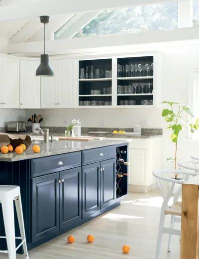 Una cocina pintada de blanco con armarios blancos y armarios de la isla de color gris azulado oscuro.