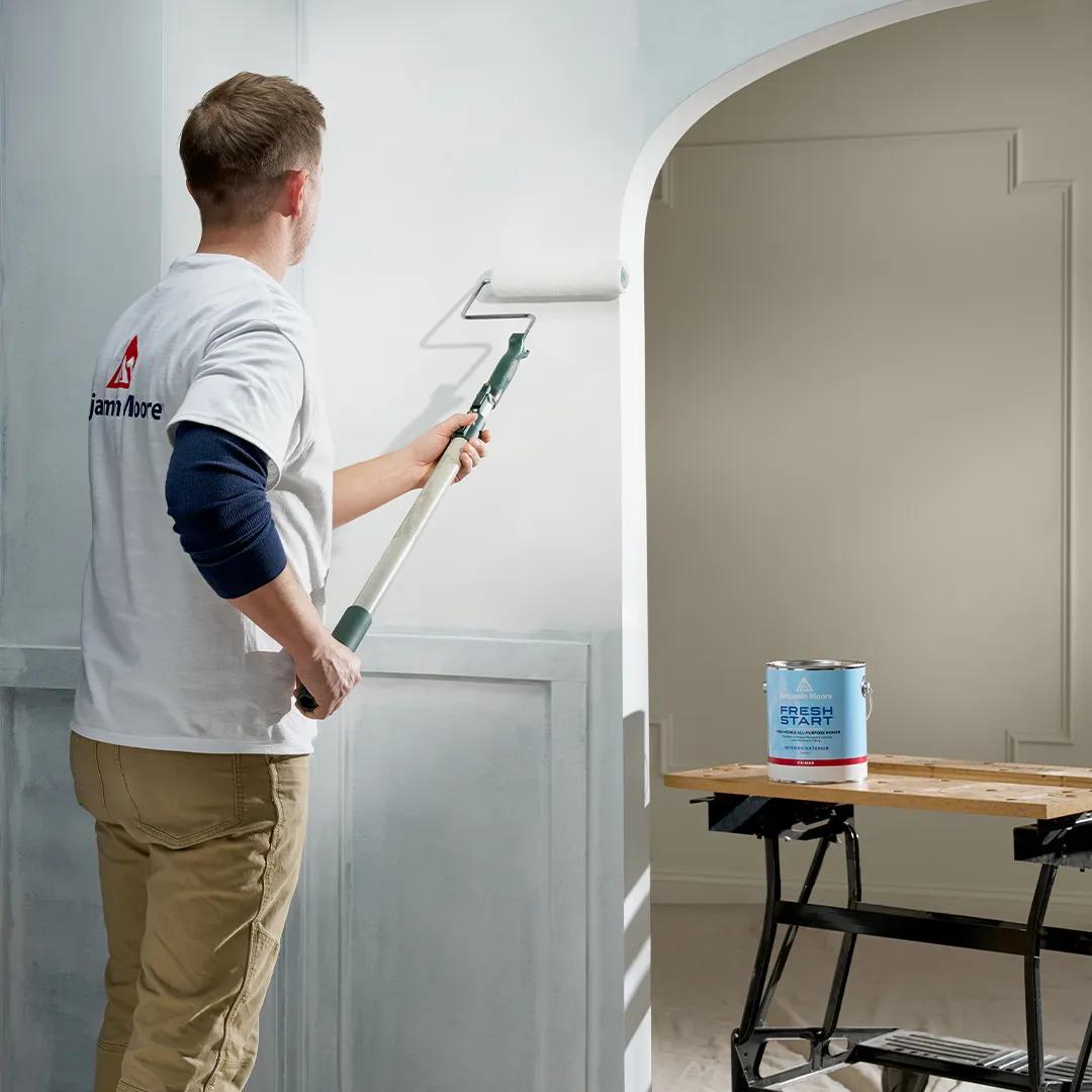 Un hombre aplicando imprimador sobre una pared blanca cubierta de marcas de crayón.