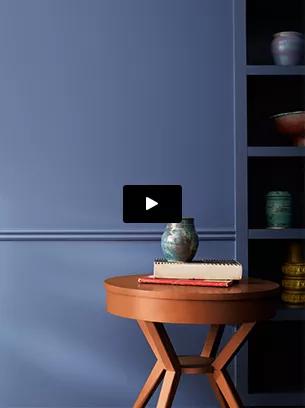 Una mesa moderna circular de cerezo sostiene un jarrón Azul y libros frente a una pared pintada de Azul de Nova.