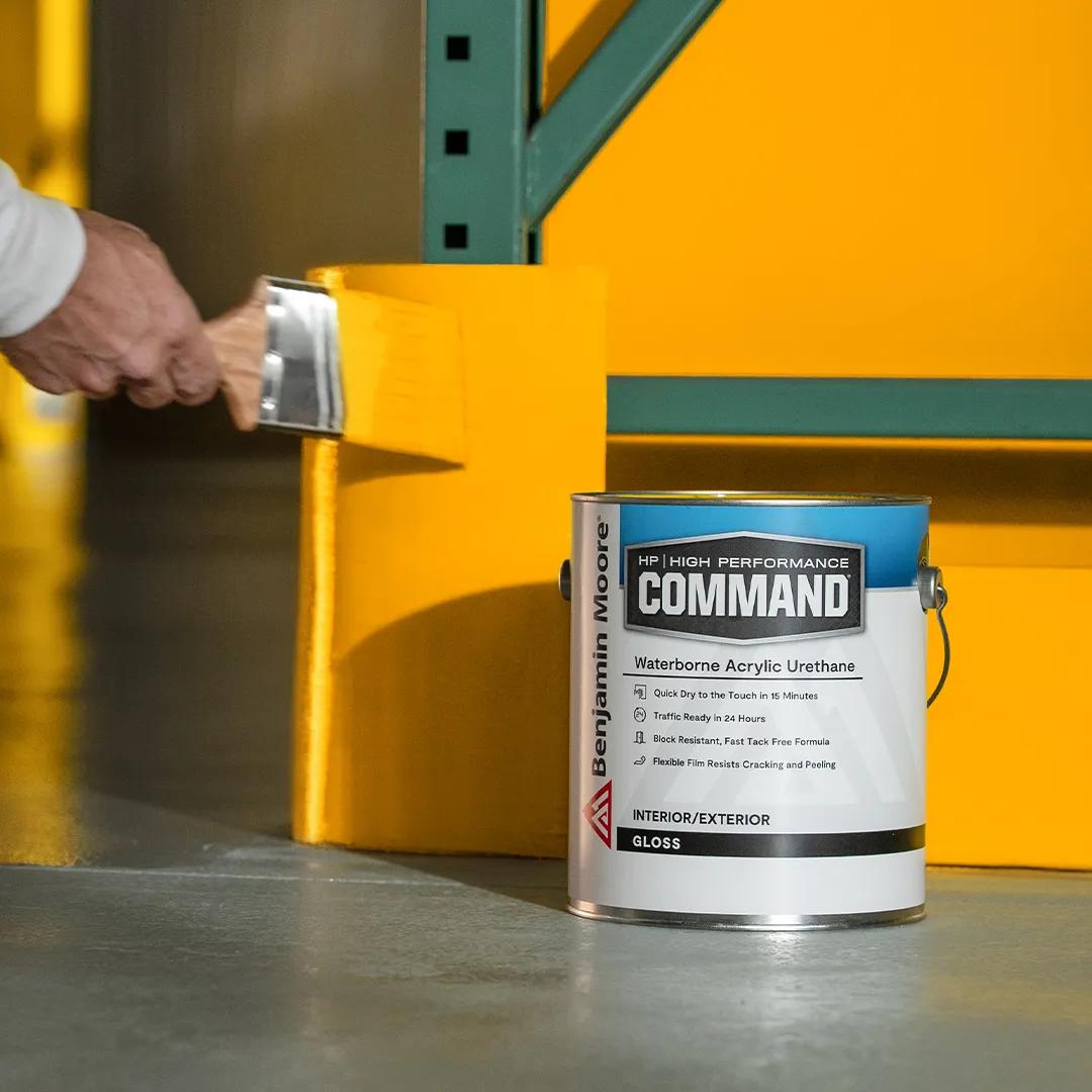 Una persona pintando con brocha una sección de pared de color naranja detrás de una lata de 1 galón de Command® Uretano acrílico al agua de Benjamin Moore.