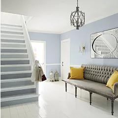 Miniatura: Un vestíbulo pintado en blanco y gris con una escalera de dos tonos, pisos blancos y decoración ecléctica.