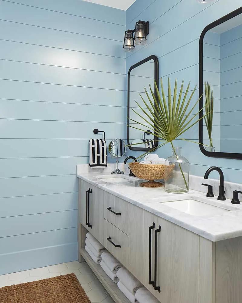 Un baño con paredes traslapadas pintadas de azul y un tocador doble de madera rubia.