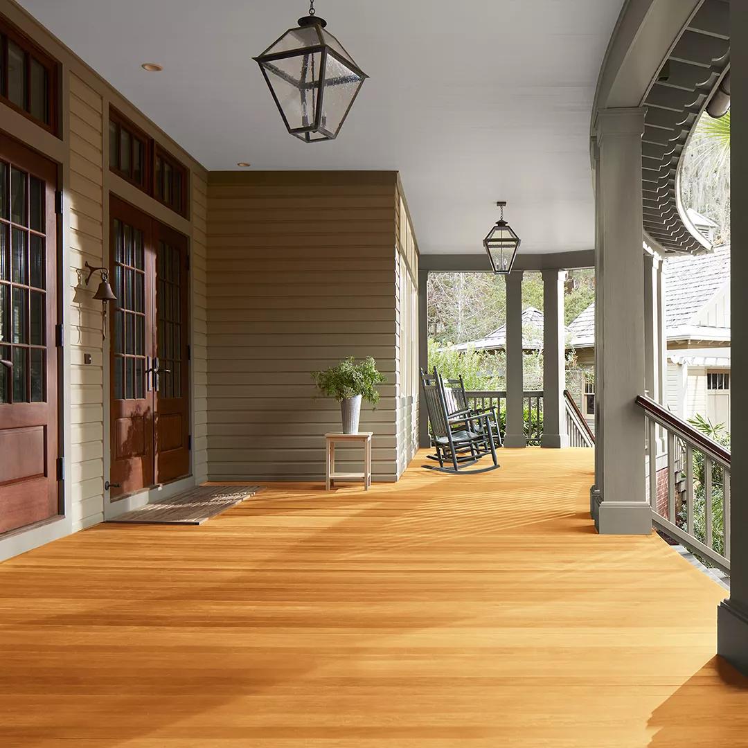 Miniatura de un espacioso porche delantero cubierto con revestimientos exteriores pintados de color beige, columnas de color verde apagado y techo blanco, que cuenta con hermosas puertas principales y piso teñido con Woodluxe® Tinte para exteriores Traslúcido en Natural ES-10.