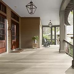 Miniatura de un espacioso porche delantero cubierto con revestimientos exteriores pintados de color Beige, columnas de color Verde apagado y techo Blanco, cuenta con un hermoso piso y puertas principales con Woodluxe® Tinte para exteriores traslúcido en Gris Blanquecino ES-78.