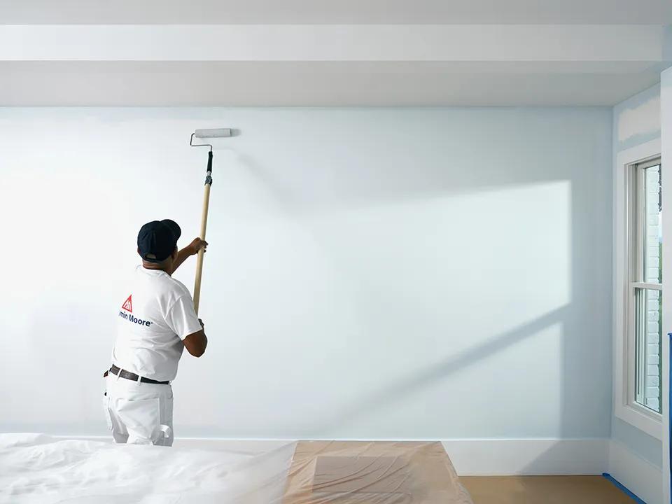 Un pintor pasa el rodillo con pintura color Estanque Tranquilo sobre una pared en una habitación blanca.