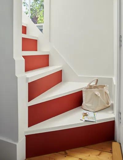 Una escalera con contrahuellas pintadas de rojo y peldaños blancos entre paredes blancas.