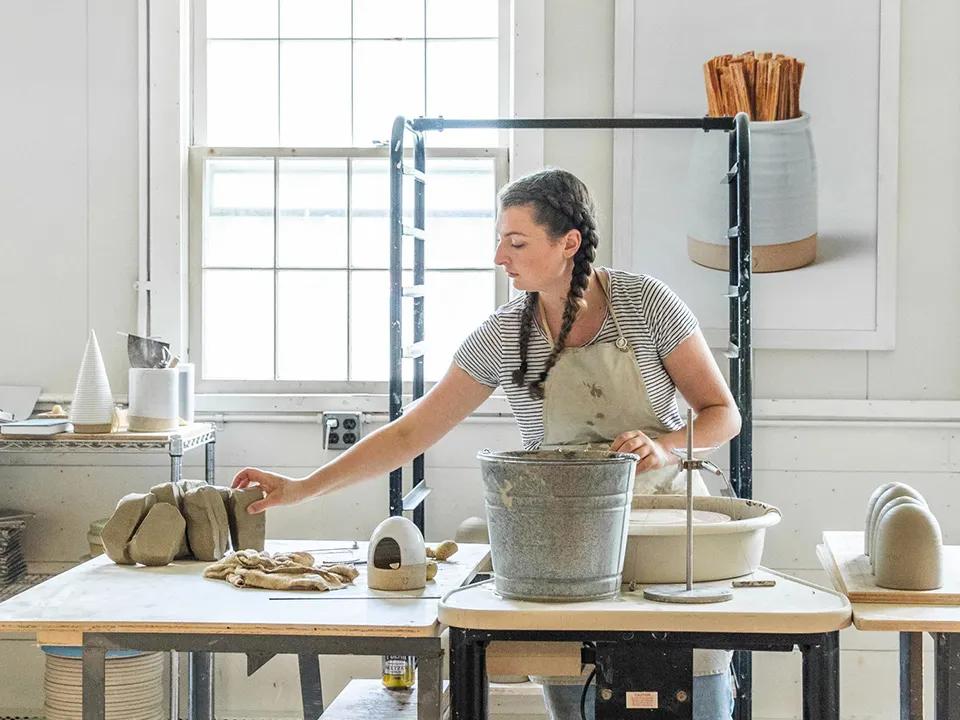 Una alfarera trabaja en una mesa dentro del taller de Farmhouse Pottery.
