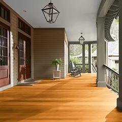 Miniatura de un espacioso porche delantero cubierto con revestimientos exteriores pintados de color beige, columnas de color verde apagado y techo blanco, que cuenta con hermosas puertas principales y piso teñido con Woodluxe® Tinte para exteriores Traslúcido en Cedro ES-40.