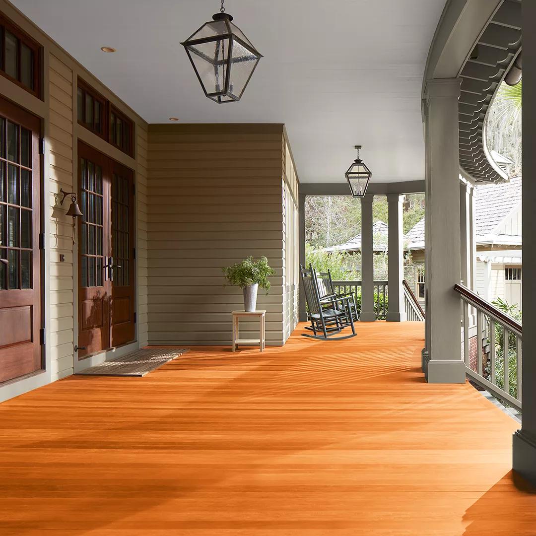 Un espacioso porche delantero cubierto con revestimientos exteriores pintados de color beige, columnas de color verde apagado y techo blanco, que cuenta con hermosas puertas principales y piso teñido con Woodluxe® Tinte para exteriores Traslúcido en Redwood ES-20.