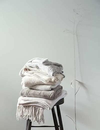 Una pared pintada de blanco impuro con un taburete apilado con ropa doblada.