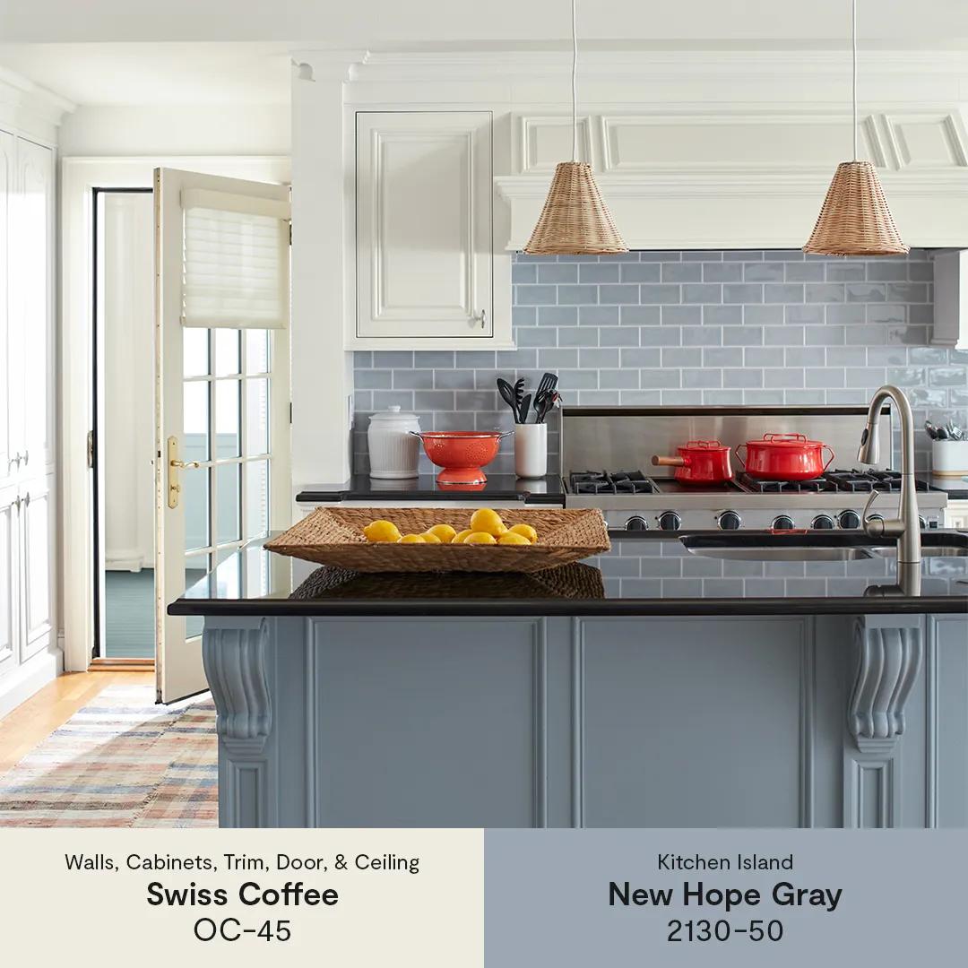 A white painted kitchen with an open back door, a blue-gray painted island with a black countertop, and a gray tile backsplash.
