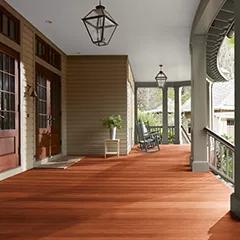 Miniatura de un espacioso porche delantero cubierto con revestimientos exteriores pintados de color beige, columnas de color verde apagado y techo blanco, que cuenta con hermosas puertas principales y piso teñido con Woodluxe® Tinte para exteriores Traslúcido en Caoba ES-60.